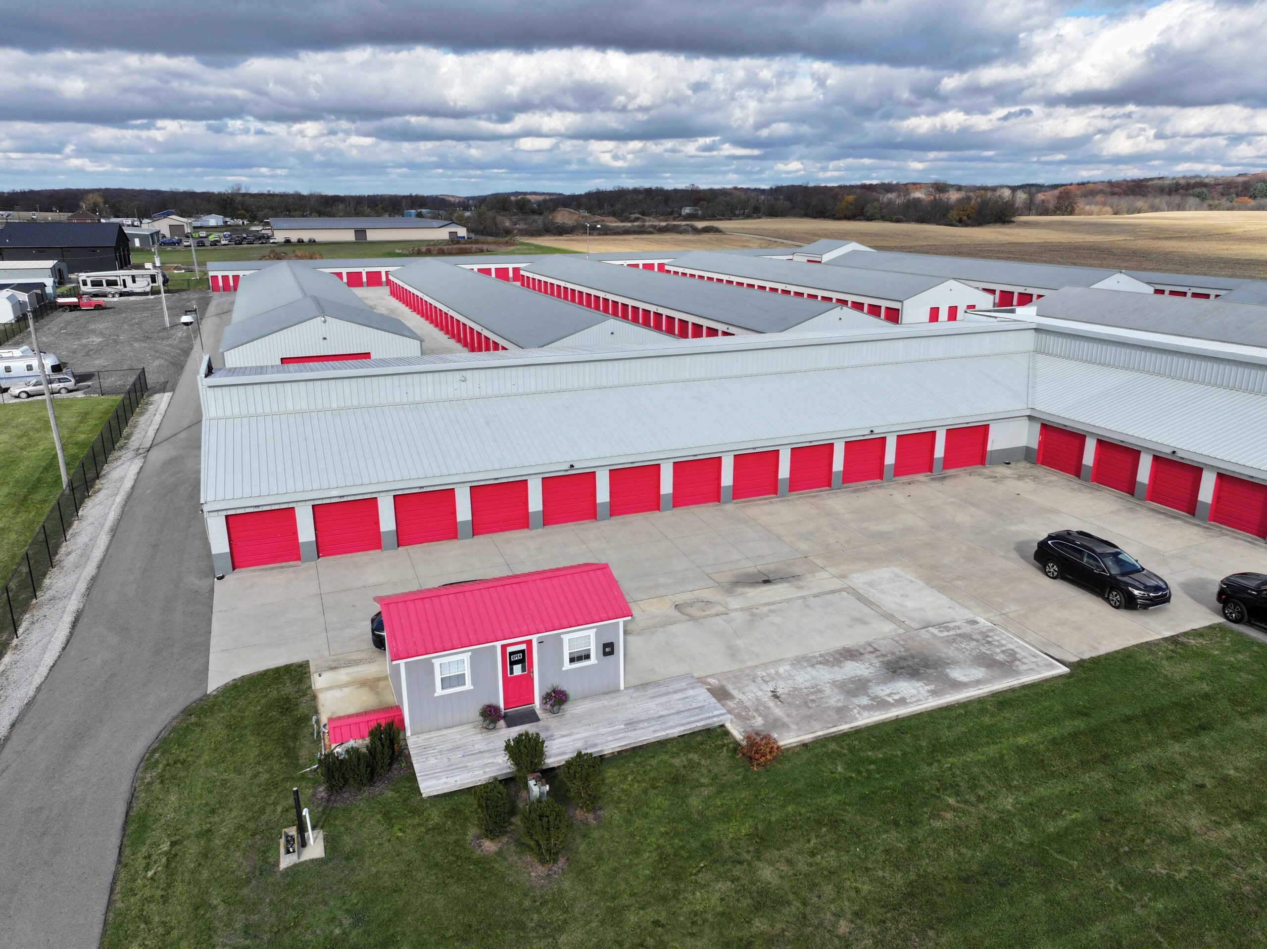 Aerial view of a self-storage facility in Angola featuring rows of red and gray storage units with ample drive-up access. The facility is surrounded by open fields, highlighting a spacious and secure environment for storing belongings.